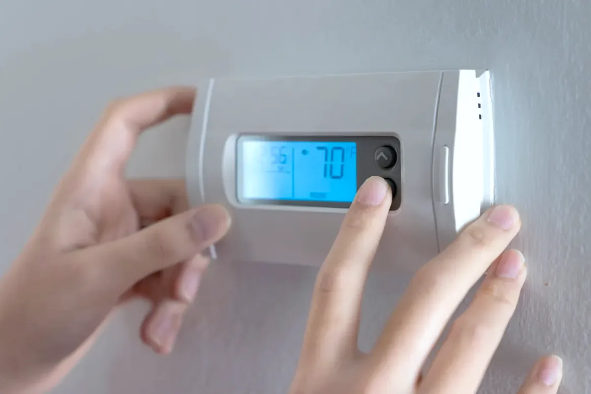 Hands adjusting a digital wall thermostat